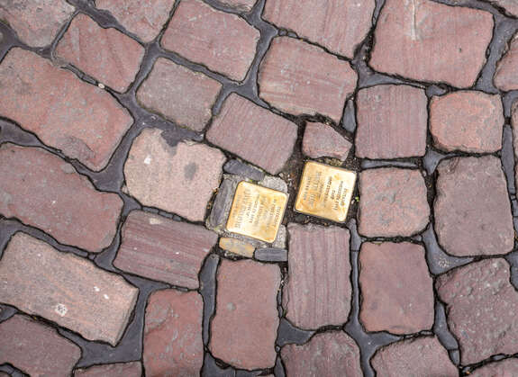 Goldene Stolpersteine, die in einen Weg aus Pflastersteinen eingelassen sind