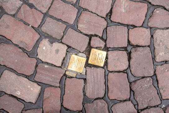 Goldene Stolpersteine, die in einen Weg aus Pflastersteinen eingelassen sind