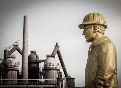 Eine goldene Bergmannssulptur, im Hintergrund Hüttengelände