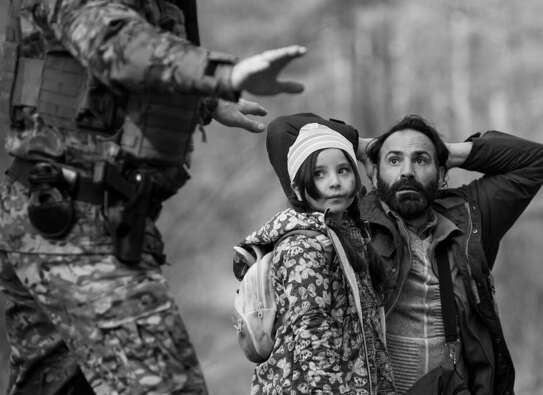 Filmszene. Ein Vater kniet mit erhobenen Händen auf dem Boden, daneben seine Tochter. Ein Soldat hält seine Hand schützend über beide.