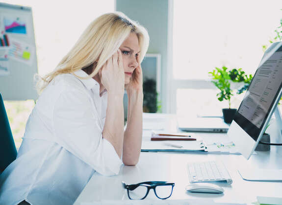 Frau, die vor einem Computer sitzt und sehr angestrengt aussieht. 