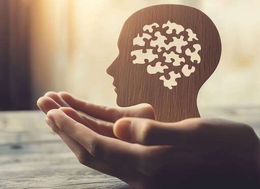 Hand hält eine Siluette von einem Kopf mit vielen Puzzleteilen