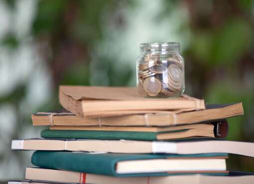 Glas mit Geldmünzen, dass auf einem Stapel Lehrbücher steht Glas mit Geldmünzen, dass auf einem Stapel Lehrbücher steht